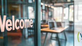 Glaswand mit dem Wort ‚Welcome‘ in großen Buchstaben; daneben das Logo des Welcome Center KMU Rheinisches Revier mit den Buchstaben ‚WCR‘ und dem Text ‚Welcome Center KMU Rheinisches Revier‘ auf unscharfem Bürohintergrund.