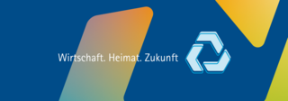 Blauer Hintergrund mit farbigen Sechsecken und weißem Text ‚Wirtschaft. Heimat. Zukunft.‘ in der Mitte. Rechts daneben ein hellblaues Symbol aus drei Pfeilen in Kreisform.