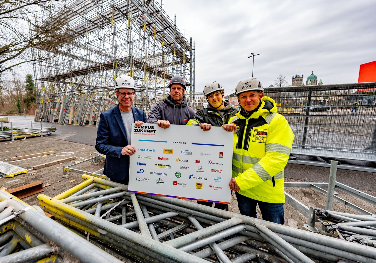 Auf dem Wendersplatz errichtet die Firma Gerüstbau Kaiser die Pavillon-Konstruktion für den Campus Zukunft. IHK-Hauptgeschäftsführer Jürgen Steinmetz,  Jens Krebs (Obermonteur und Vorarbeiter), Justin Kaiser (Auszubildender) und Oliver Hampel (Geschäftsführer von Gerüstbau Kaiser, v.l.) zeigen eine Übersicht über die Partner des Projekts.