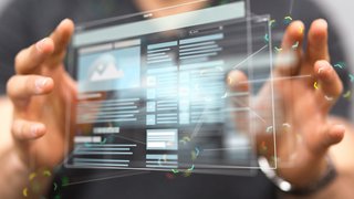 Eine Person hält ein transparentes, holografisches Display mit beiden Händen. Das Display zeigt eine Benutzeroberfläche mit mehreren Textblöcken, Bildern und Menüs. Die Hände der Person sind leicht unscharf im Vordergrund zu sehen, während das Display scharf und detailliert dargestellt ist.