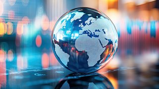 Glänzende Glaskugel mit digitaler Weltkarte, die Europa, Afrika und Teile Asiens zeigt, steht auf einer spiegelnden Oberfläche; im Hintergrund unscharfe bunte Lichter und ein digitales Börsendiagramm.