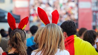 Mehrere Personen von hinten bei einer Veranstaltung, einige tragen rote Hasenohren und eine schwarz-rot-goldene Flagge ist im Bild zu sehen.