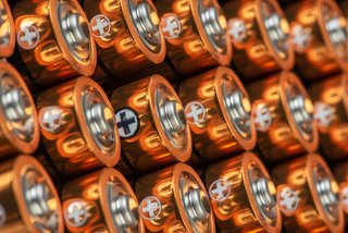 Nahaufnahme mehrerer AA-Batterien mit sichtbarem Pluspol, in gleichmäßigen Reihen angeordnet.