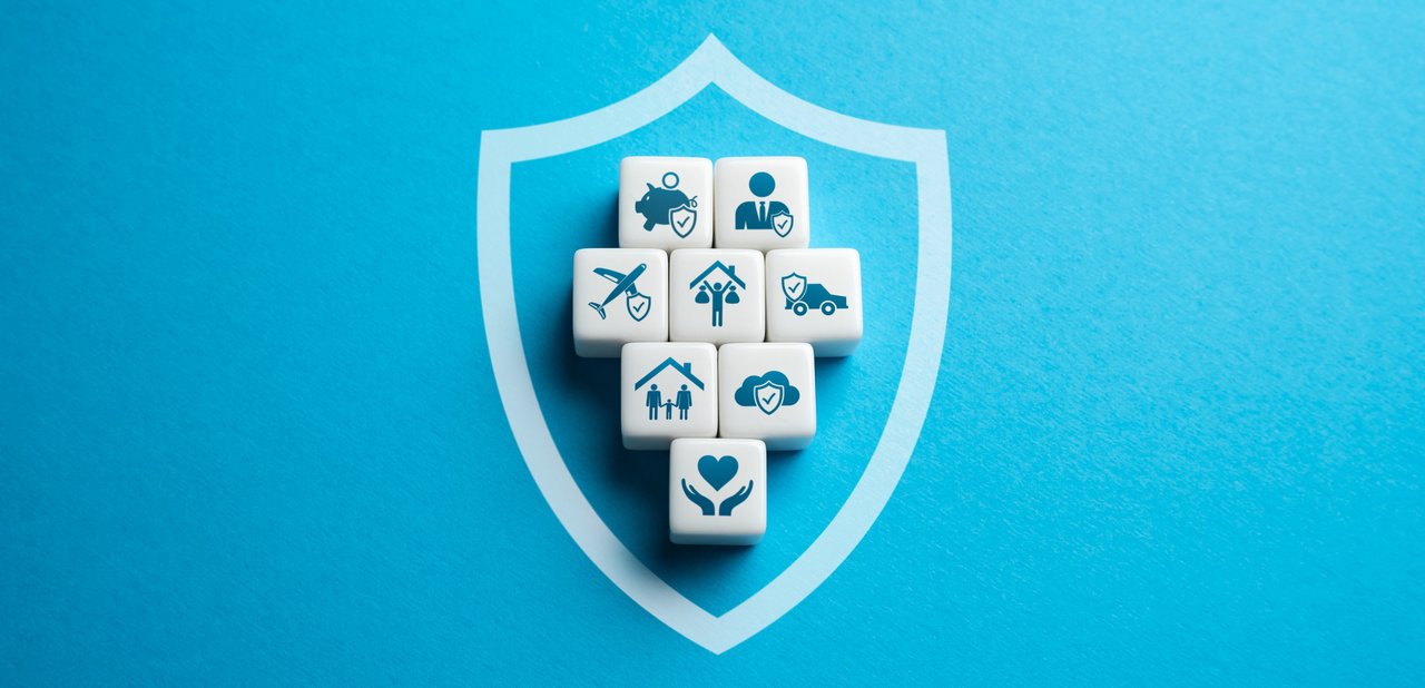 Weiße Würfel mit blauen Symbolen, die verschiedene Versicherungsbereiche darstellen – darunter Gesundheit, Familie, Reisen, Haus, Auto, Finanzen und Cloud – sind in Form eines Pluszeichens auf einem blauen Hintergrund mit einem stilisierten Schutzschild platziert, das Sicherheit und Schutz symbolisiert.