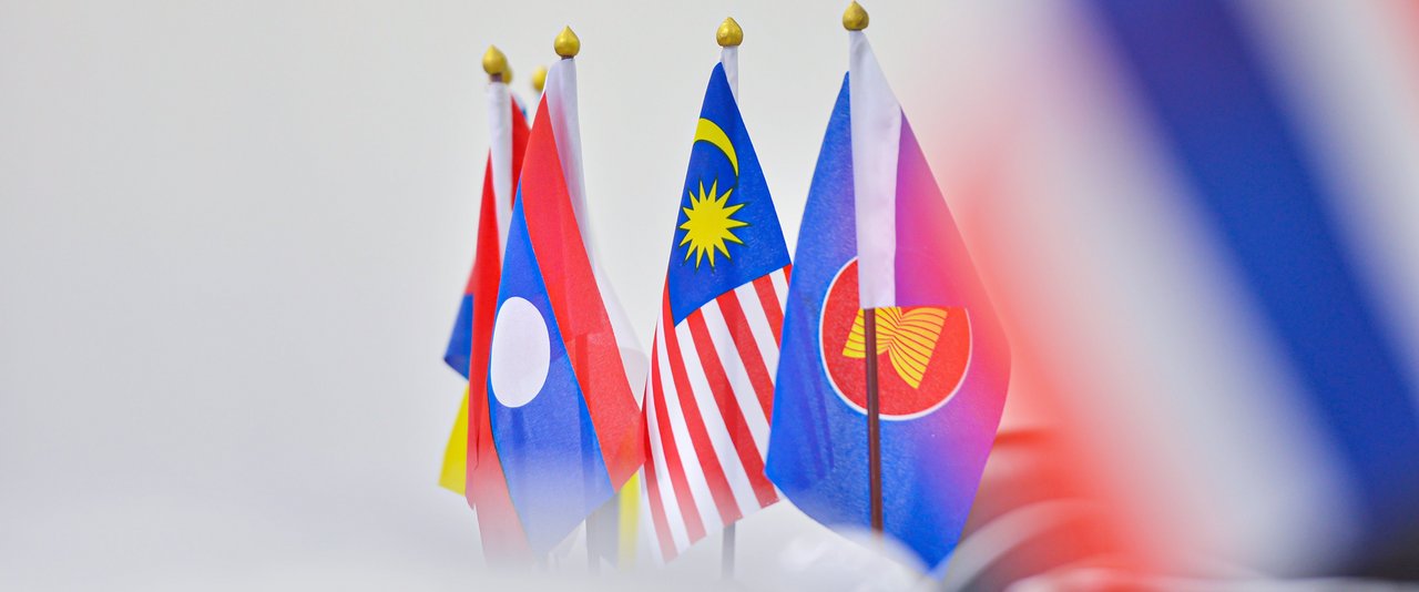 Nationalflaggen von Laos, Malaysia und der ASEAN in einer Reihe, scharf im Vordergrund, mit unscharfem Hintergrund.