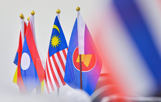 Nationalflaggen von Laos, Malaysia und der ASEAN in einer Reihe, scharf im Vordergrund, mit unscharfem Hintergrund.