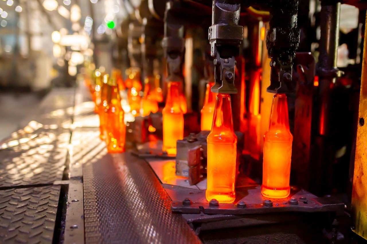 Glühend heiße Glasflaschen werden in einer Fabrikreihe geformt und von Maschinenarmen gehalten.