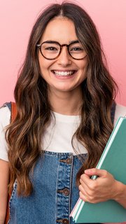 Lächelnde junge Frau mit langen braunen Haaren, Brille und Jeanskleid steht vor einem rosa Hintergrund. Sie trägt einen braunen Lederrucksack und hält Hefte oder Ordner in der Hand.