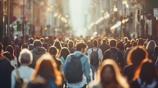 Viele Menschen gehen auf einer belebten Einkaufsstraße in einer Innenstadt. Die Aufnahme zeigt die Menschenmenge im warmen Gegenlicht.