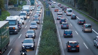 Dichter Verkehr auf einer Autobahn mit mehreren Fahrspuren in beide Richtungen; auf der linken Seite staut sich der Verkehr, während auf der rechten Seite die Fahrzeuge langsam fließen.