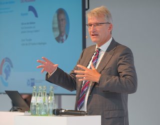 Elmar Theveßen spricht an einem Rednerpult während des Strategieforum Außenwirtschaft 2024; im Hintergrund ist eine Leinwand mit Programmhinweisen zu sehen.