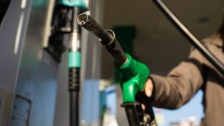 Hand hält eine grüne Zapfpistole an einer Tankstelle beim Betanken eines Fahrzeugs.