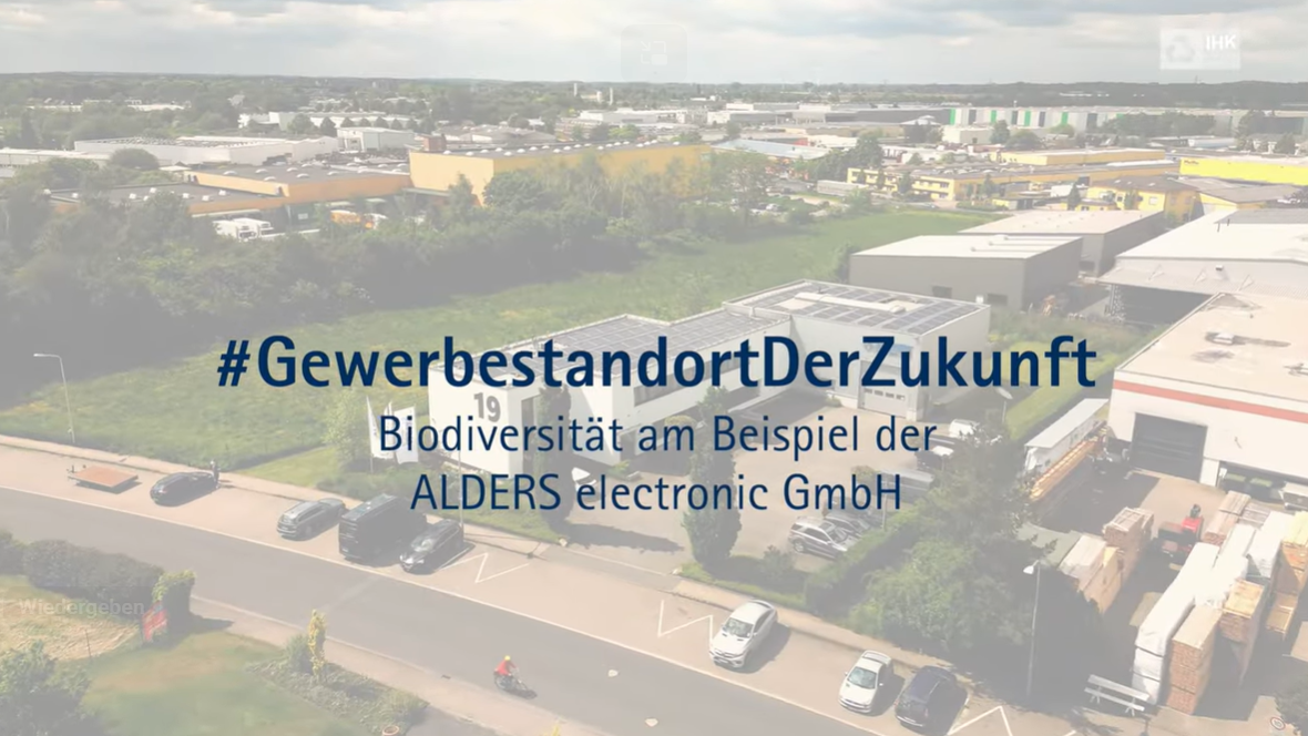 Luftaufnahme eines Gewerbegebiets mit Firmengebäuden und Straßen, überlagert mit dem Text „#GewerbestandortDerZukunft – Biodiversität am Beispiel der ALDERS electronic GmbH“.