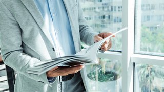 businessman in a business suit reads a magazine near the window with a plant