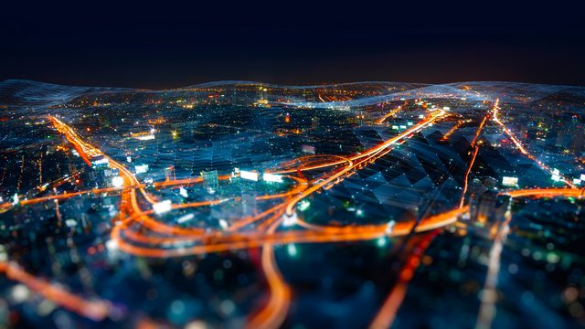 Nächtliche Stadtansicht aus der Vogelperspektive mit leuchtenden Straßen und Autobahnen, die sich durch ein weitläufiges urbanes Gebiet ziehen; die Beleuchtung betont die Verkehrswege in einem Netzwerk aus Infrastruktur und digitaler Vernetzung.