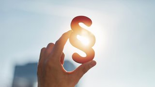 Hand hält ein Paragraphenzeichen (§) vor der Sonne, Symbol für Recht und Gesetz.