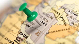 Nahaufnahme einer Landkarte des Nahen Ostens. Eine grüne Stecknadel markiert den Iran auf der Karte, nahe der Beschriftung der Hauptstadt Teheran. Umliegende Länder wie Kuwait, Afghanistan und Pakistan sind ebenfalls auf der Karte erkennbar.