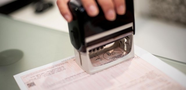 Eine Hand drückt einen großen Stempel auf ein Ursprungszeugnis, wodurch ein Siegel sichtbar wird.