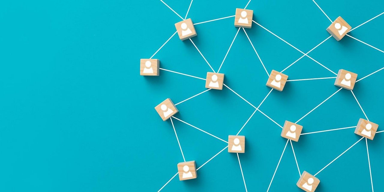 Darstellung eines Netzwerks auf blauem Hintergrund: Holzklötzchen mit weißen Personensymbolen sind durch weiße Linien miteinander verbunden, was ein soziales oder digitales Netzwerk symbolisiert.