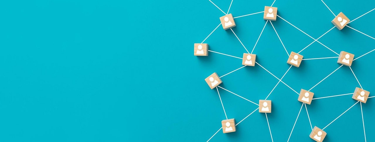 Darstellung eines Netzwerks auf blauem Hintergrund: Holzklötzchen mit weißen Personensymbolen sind durch weiße Linien miteinander verbunden, was ein soziales oder digitales Netzwerk symbolisiert.