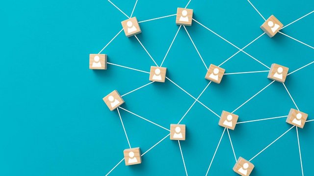 Darstellung eines Netzwerks auf blauem Hintergrund: Holzklötzchen mit weißen Personensymbolen sind durch weiße Linien miteinander verbunden, was ein soziales oder digitales Netzwerk symbolisiert.