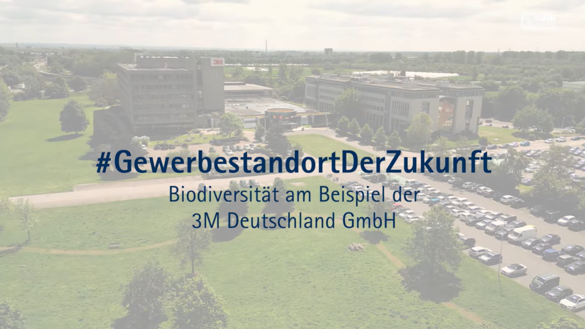Luftaufnahme eines Unternehmensstandorts mit Bürogebäuden und Parkplätzen, überlagert mit dem Text „#GewerbestandortDerZukunft – Biodiversität am Beispiel der 3M Deutschland GmbH“.