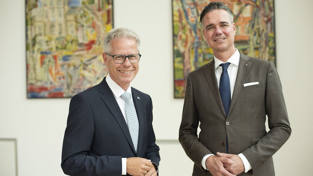 Jürgen Steinmetz, Hauptgeschäftsführer der IHK, und Elmar te Neues, Präsident der IHK, stehen nebeneinander vor einem hellen Hintergrund. Beide tragen dunkle Anzüge, weiße Hemden und hellblaue Krawatten und blicken freundlich in die Kamera.