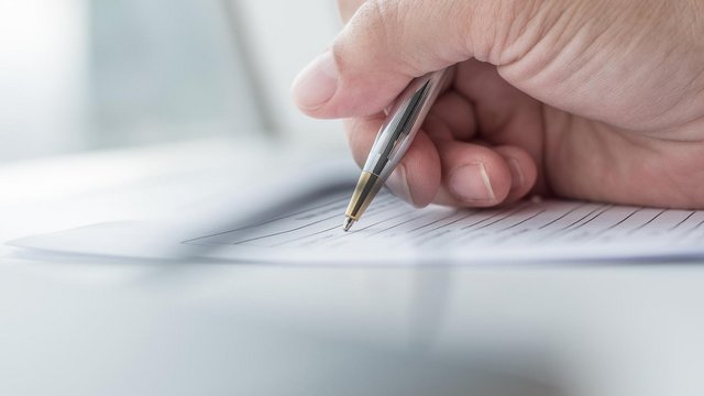 Eine Hand hält einen Kugelschreiber und schreibt auf ein Formular mit Linien.