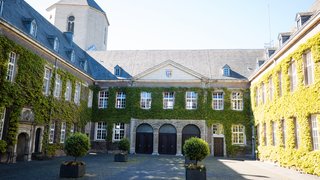Innenhof des Rathauses Mönchengladbach mit efeubewachsenen historischen Fassaden, Rundbogentoren und zentral platzierten Pflanzkübeln bei sonnigem Wetter.
