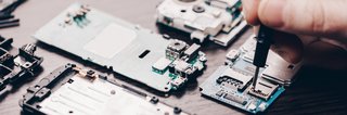 Hand montiert mit Schraubendreher eine Elektronikplatine eines zerlegten Smartphones auf einem Tisch.