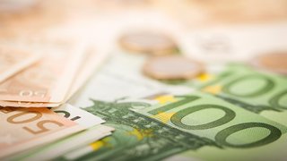 Nahaufnahme von Euro-Banknoten in verschiedenen Stückelungen, darunter 50- und 100-Euro-Scheine, sowie einige unscharf dargestellte Euromünzen im Hintergrund. Das Bild vermittelt ein Thema rund um Geld, Finanzen oder wirtschaftliche Ressourcen.