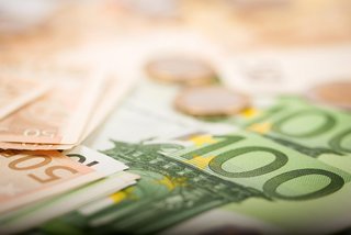 Nahaufnahme von Euro-Banknoten in verschiedenen Stückelungen, darunter 50- und 100-Euro-Scheine, sowie einige unscharf dargestellte Euromünzen im Hintergrund. Das Bild vermittelt ein Thema rund um Geld, Finanzen oder wirtschaftliche Ressourcen.