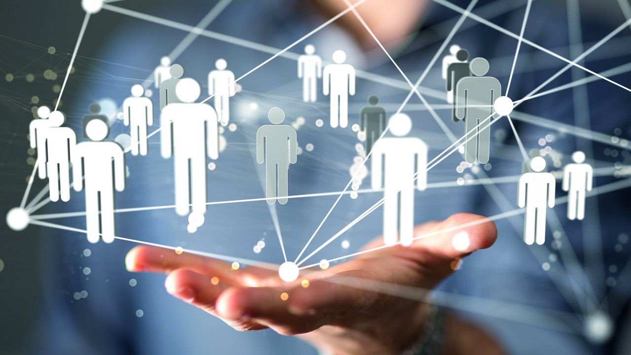 Offene Handfläche einer Person im Anzug, darüber schwebt ein Netzwerk aus verbundenen, stilisierten menschlichen Symbolen, die durch Linien und Punkte verbunden sind. Das Bild symbolisiert soziale Netzwerke, Personalmanagement oder Fachkräftesicherung im digitalen Kontext.