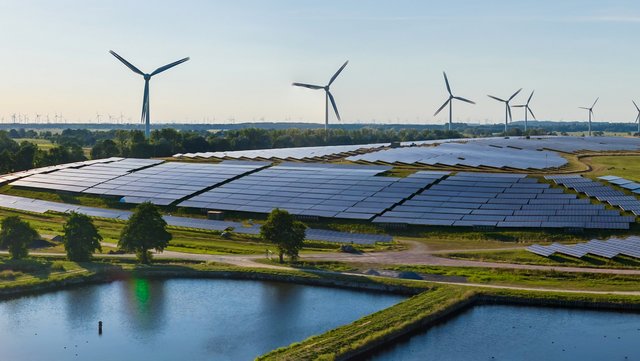 Große Solarfelder und Windkraftanlagen in einer grünen Landschaft.
